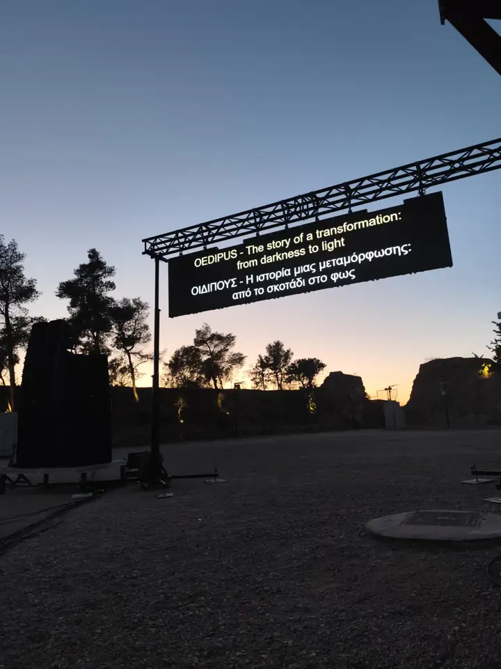 An outdoor LED screen, Greek and English titles at dusk.