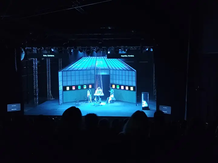 Titles on screens above a lit stage.